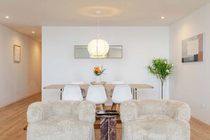 Un espace repas moderne avec une table en bois, des chaises blanches, un tapis moelleux et un luminaire suspendu.