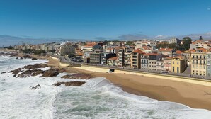 Paisagem costeira com uma praia de areia, um calçadão e diversos edifícios.