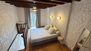 Un dormitorio con techo de madera, una cama con ropa de cama blanca, una mesita de noche, un espejo y vistas al exterior a través de una ventana.