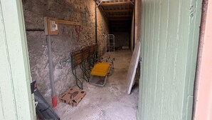 Un estrecho pasillo con piso de concreto, vigas de madera, un portaequipajes metálico y un banco amarillo.