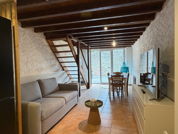 A cozy living room with a sofa, a coffee table, a TV, and a dining area with chairs and a table.