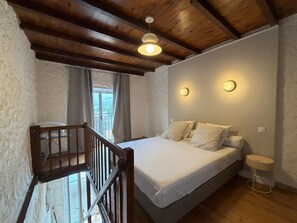 A bedroom with a wooden ceiling, a bed with white bedding, a small bedside table, and a window with curtains.