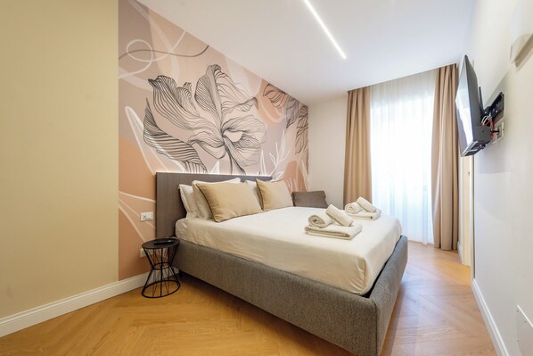 Un dormitorio moderno con una cama, una mesita y un televisor montado en la pared.