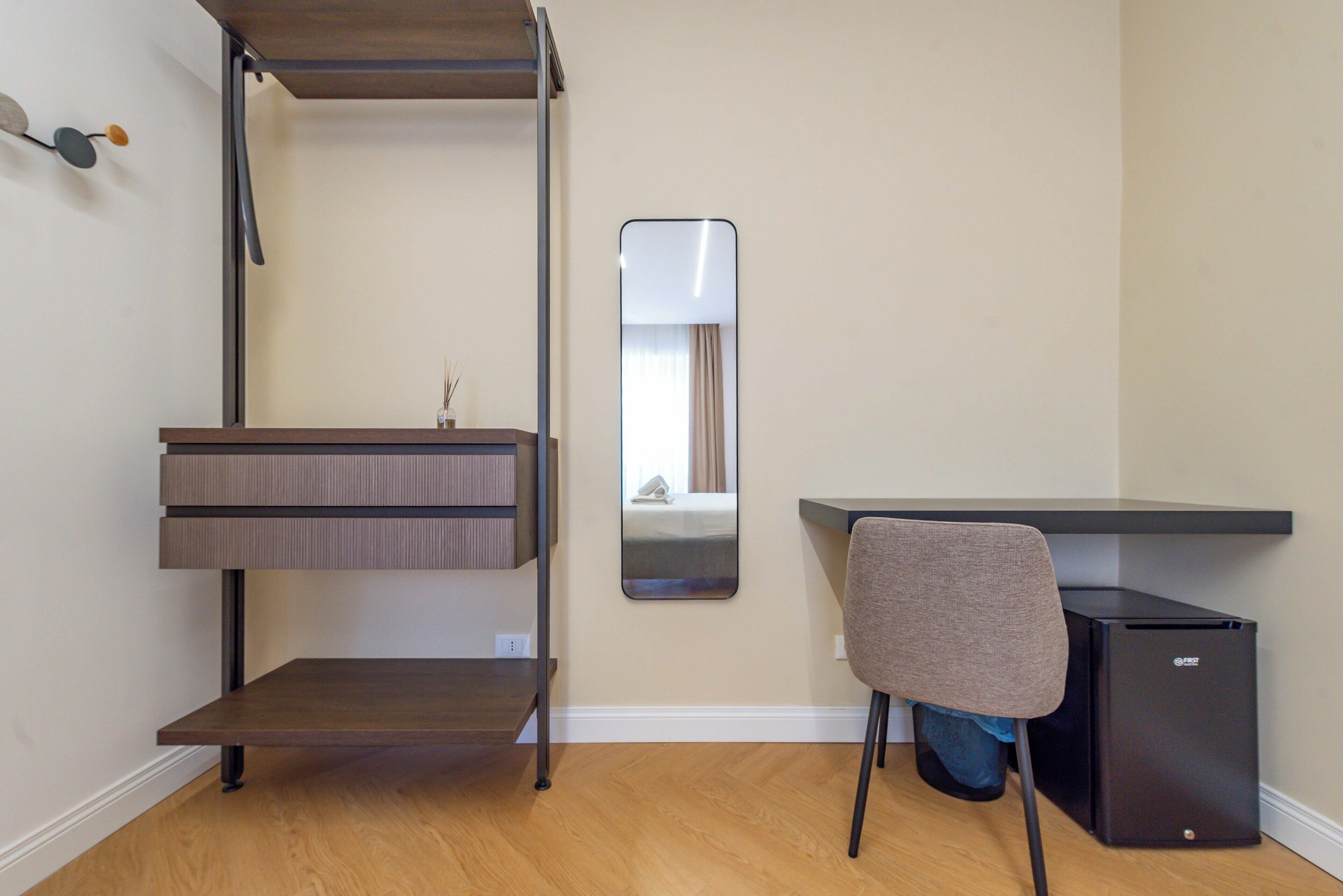 A compact room with a bunk bed, a small desk, a chair, and a mirror.