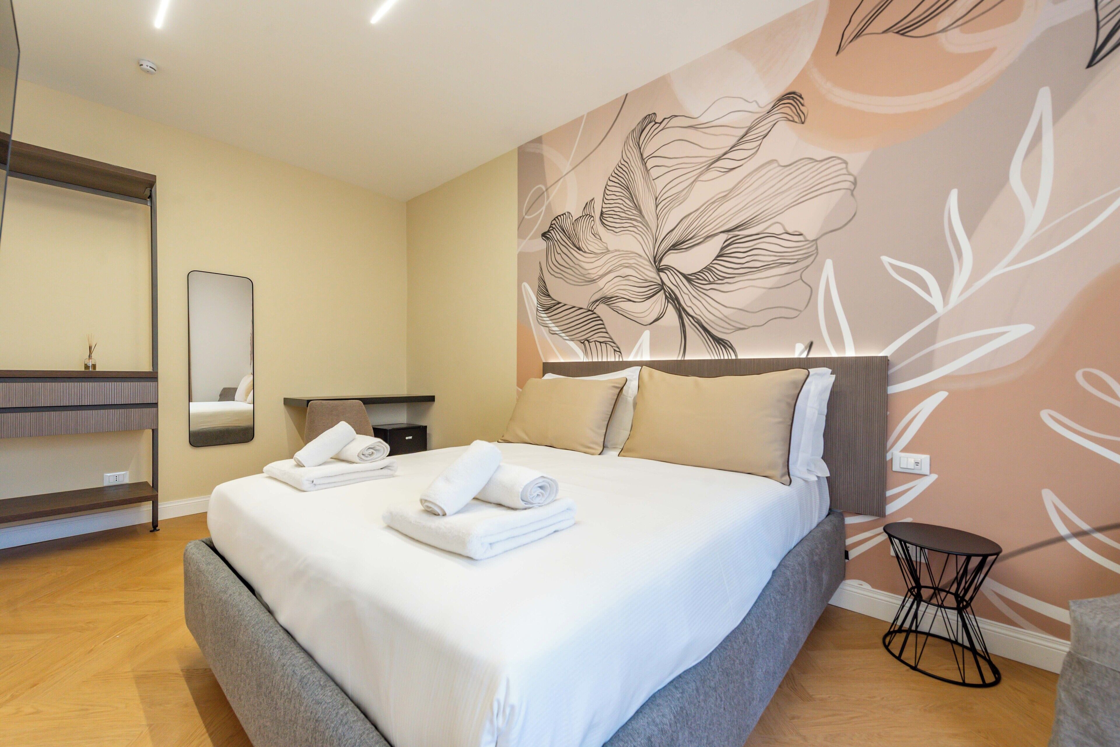 A hotel room with a large bed, a bedside table, a mirror, and a wall with a floral design.
