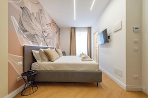 Quarto de hotel moderno com cama, TV de tela plana e termostato fixado na parede.