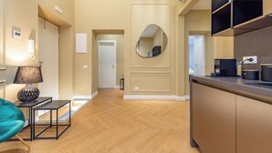 Habitación de hotel moderna con piso de madera, sofá, mesa, lámpara, espejo y kitchenette.