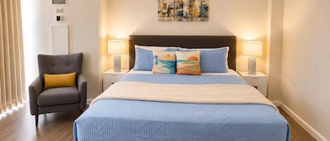A bedroom with a large bed, two bedside tables with lamps, a chair, and a wall-mounted artwork.