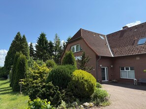 Une maison à deux étages, construite en briques et dotée d’un toit en tuiles, entourée d’une végétation bien entretenue et accessible par une allée pavée.
