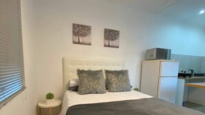 Quarto com cama, mesinha redonda, uma planta pequena, cabeceira e duas pinturas penduradas na parede.