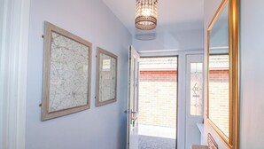 A hallway with two framed maps, a chandelier, a door with a glass panel, and a small Aston Martin model on a wooden surface. - Pinecote Cottage (Nottingham)