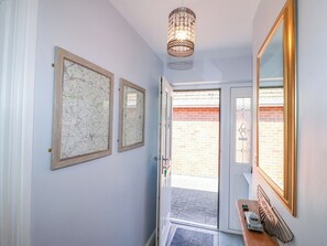 Ein Flur mit zwei gerahmten Karten, einem Chandelier, einer Tür mit Glasfenster und einem kleinen Aston Martin Modell auf einer Holzoberfläche.