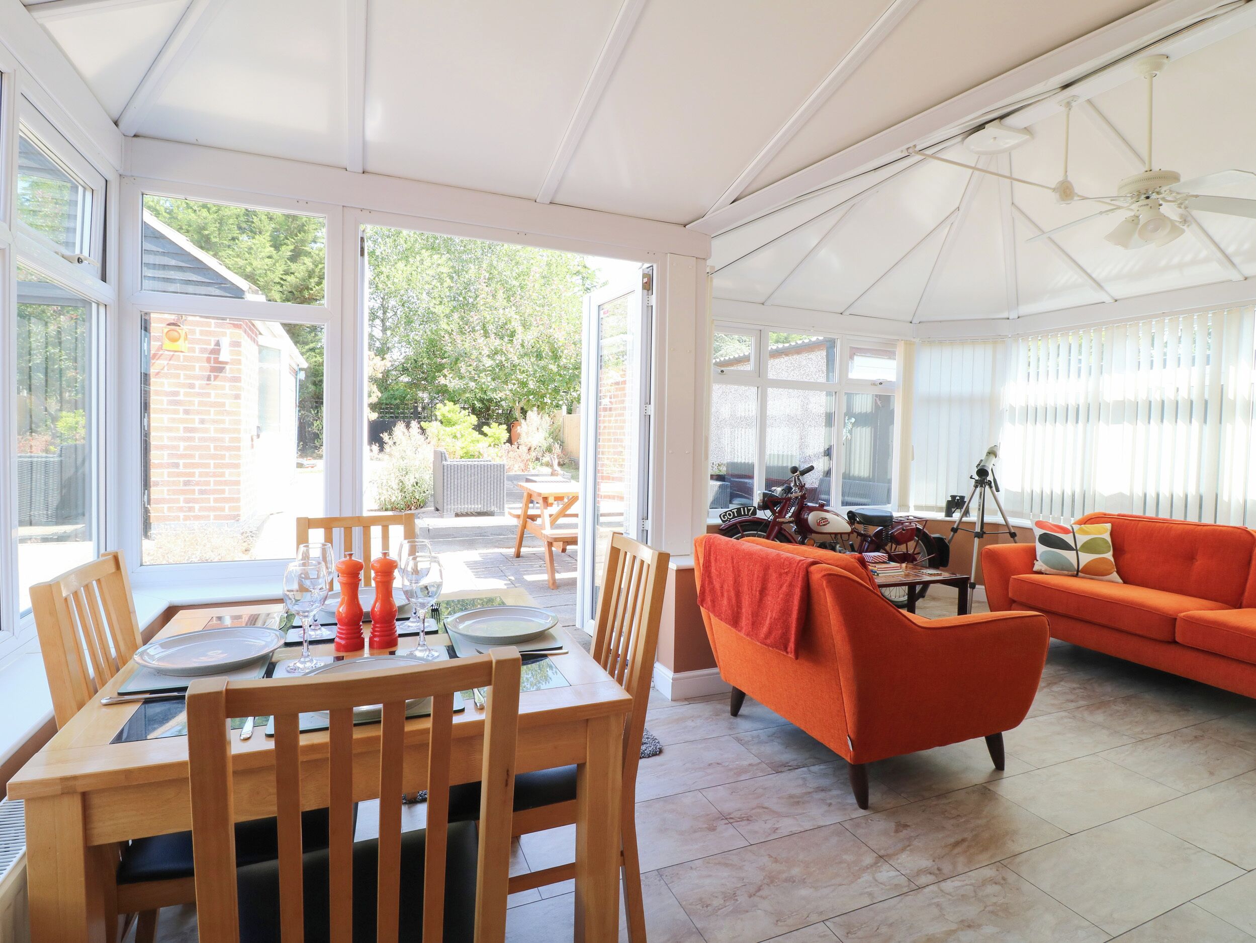A sunlit room with a dining table set for two, a sofa, and a motorcycle in the background.