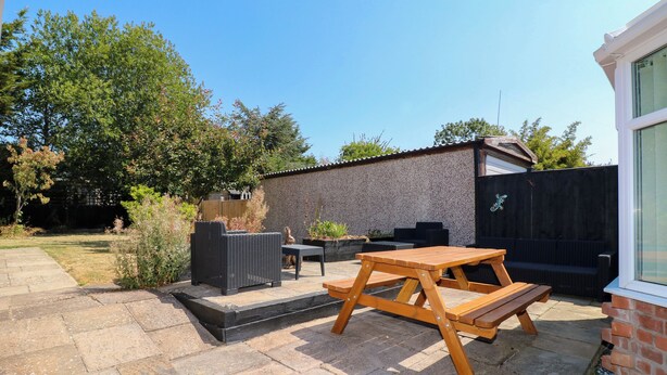 An outdoor patio with a wooden table and chairs, a black wicker sofa, and a brick wall. - Pinecote Cottage (Nottingham)