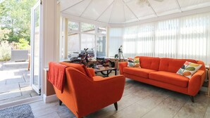 A conservatory with a ceiling fan, a red sofa, and a motorcycle. - Pinecote Cottage (Nottingham)