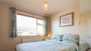 A bedroom with a bed, a window with curtains, a wall-mounted light fixture, and a framed picture. - Pinecote Cottage (Nottingham)