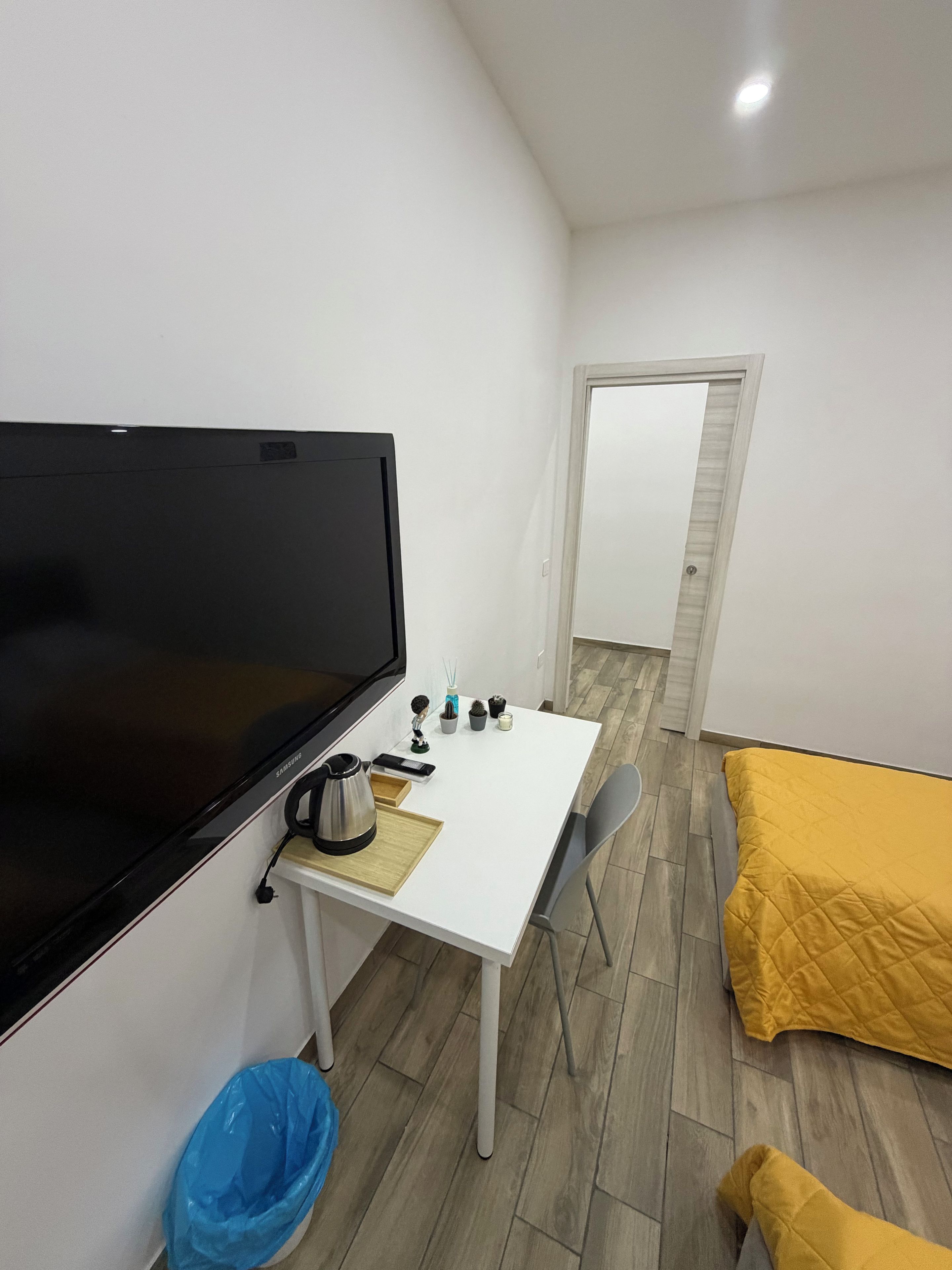 A compact room with a bed, a desk with a television, a chair, and a small trash bin.