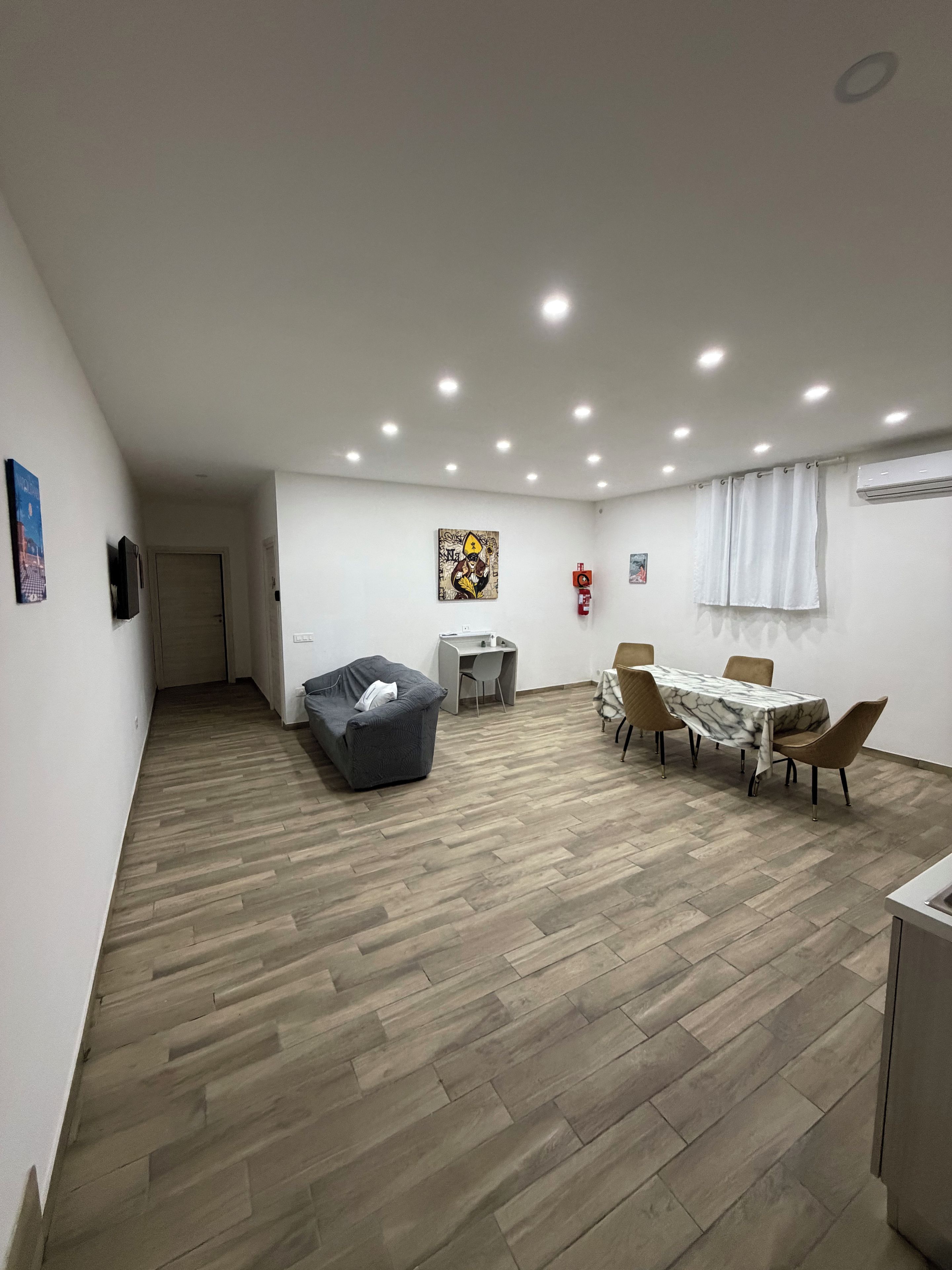 A spacious room with a dining table, chairs, a sofa, and a small desk.