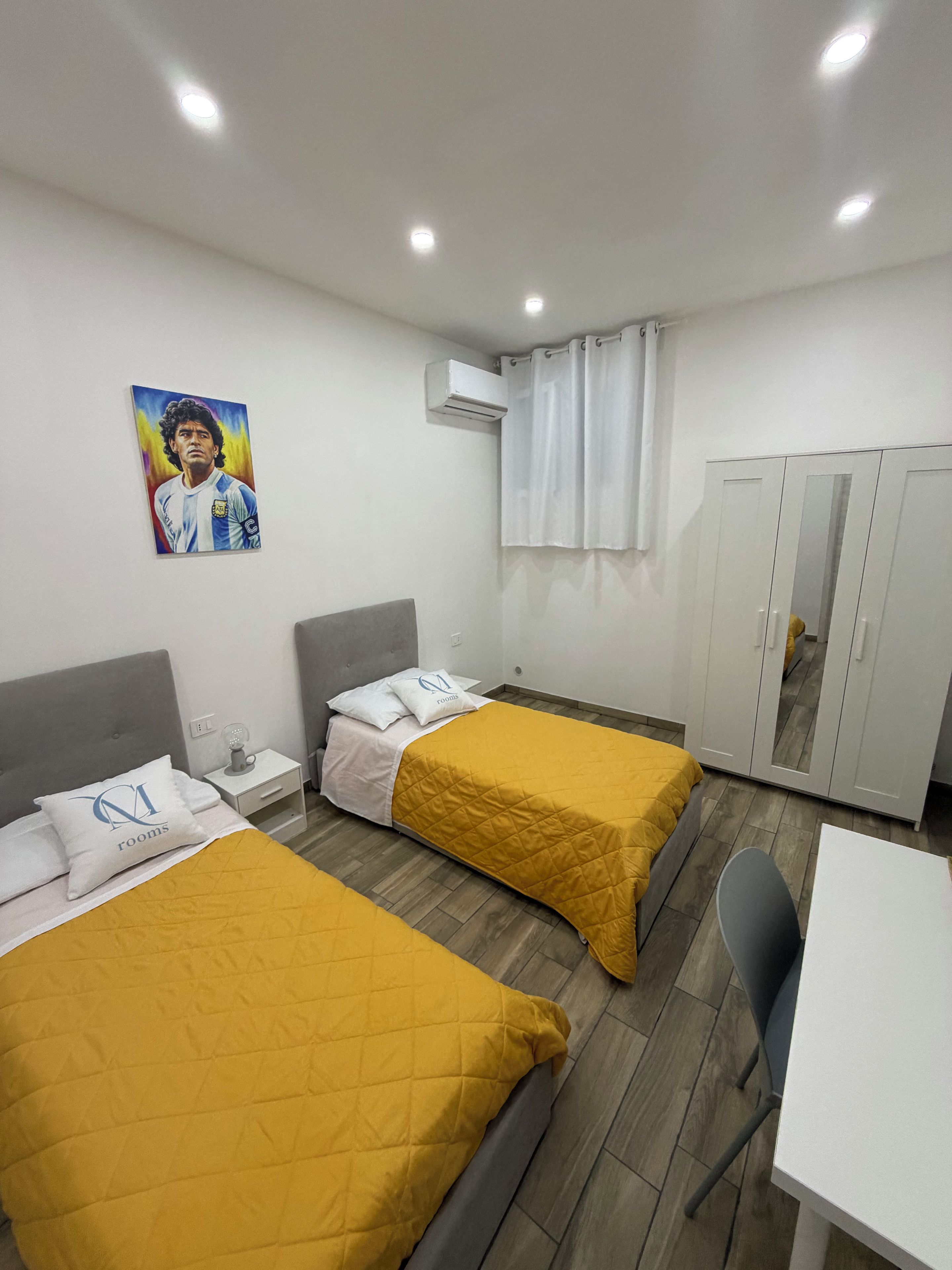 Une chambre d’hôtel avec deux lits, un bureau, une chaise, une armoire, un climatiseur et un tableau au mur.