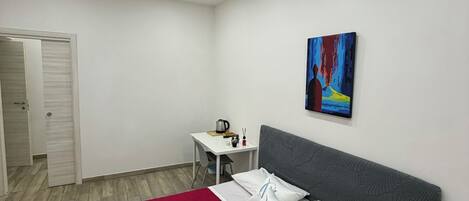 A bedroom with a bed, a desk, and a painting on the wall.
