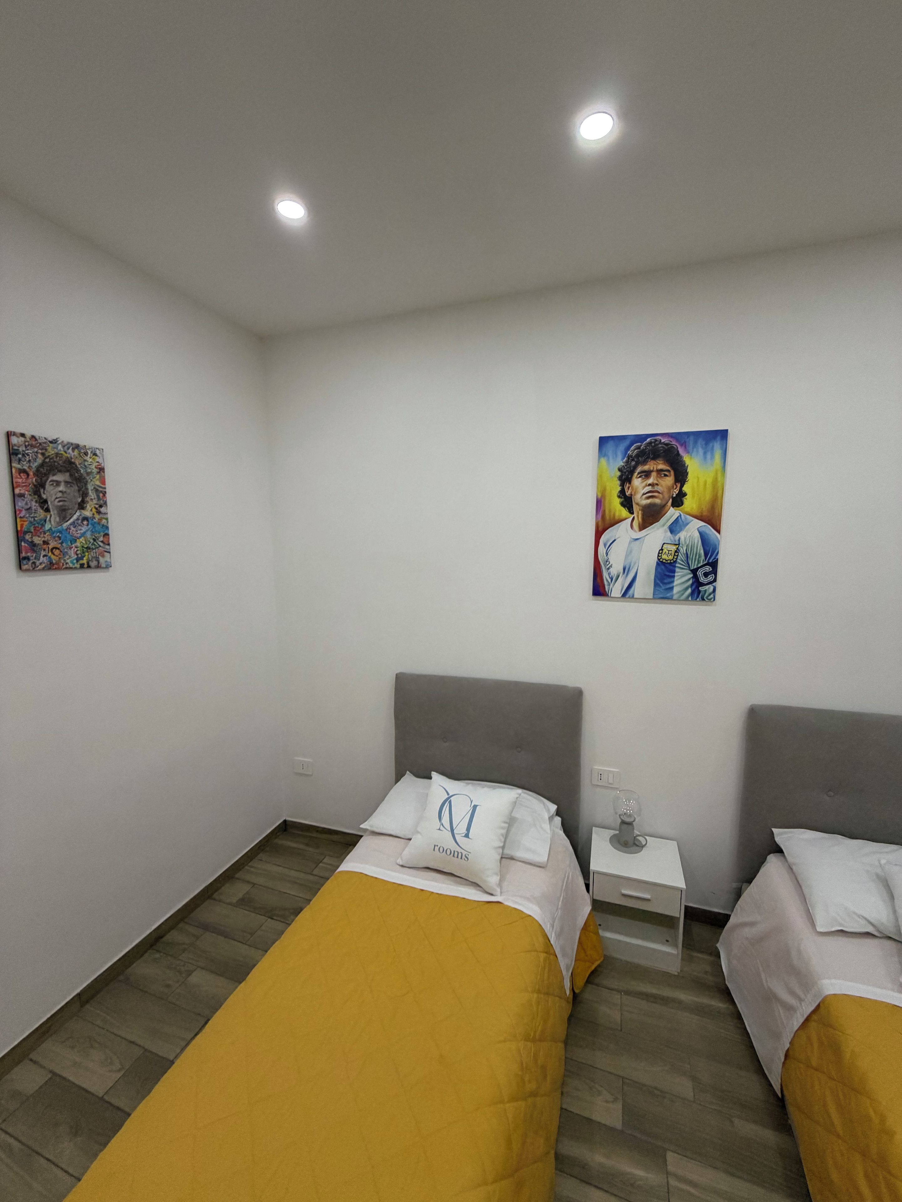 Ein Hotelzimmer mit zwei Betten, einem kleinen Nachttisch mit einem Glas und einem Bild an der Wand.
