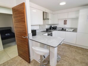 A compact kitchen with white cabinets, a countertop, a sink, and a small stool. - 4 Pump House (Birmingham)