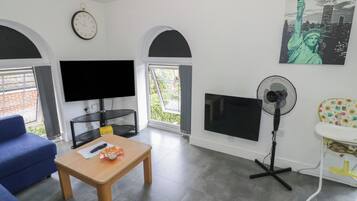 Ein Wohnzimmer mit einem blauen Sofa, einem Holztisch, einem Flachbildfernseher, einem Kamin, einem Ventilator und einem Gemälde der Freiheitsstatue.