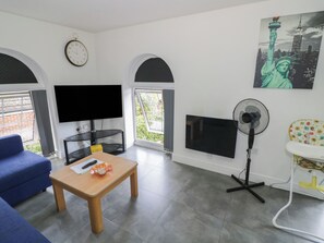 Una sala de estar con un sofá azul, una mesa de centro de madera, un televisor de pantalla plana, una chimenea, un ventilador y un cuadro de la Estatua de la Libertad.