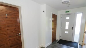 A hallway with a wooden door labeled '2', a white door with a fire exit sign, and a black mat at the entrance.