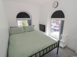 Une chambre à coucher avec un lit, un téléviseur et une fenêtre donnant sur des voitures garées.