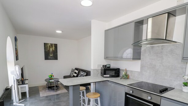 A modern kitchen with a built-in microwave, oven, and stainless steel appliances. There is a small island with stools and a seating area with a couch and pillows.