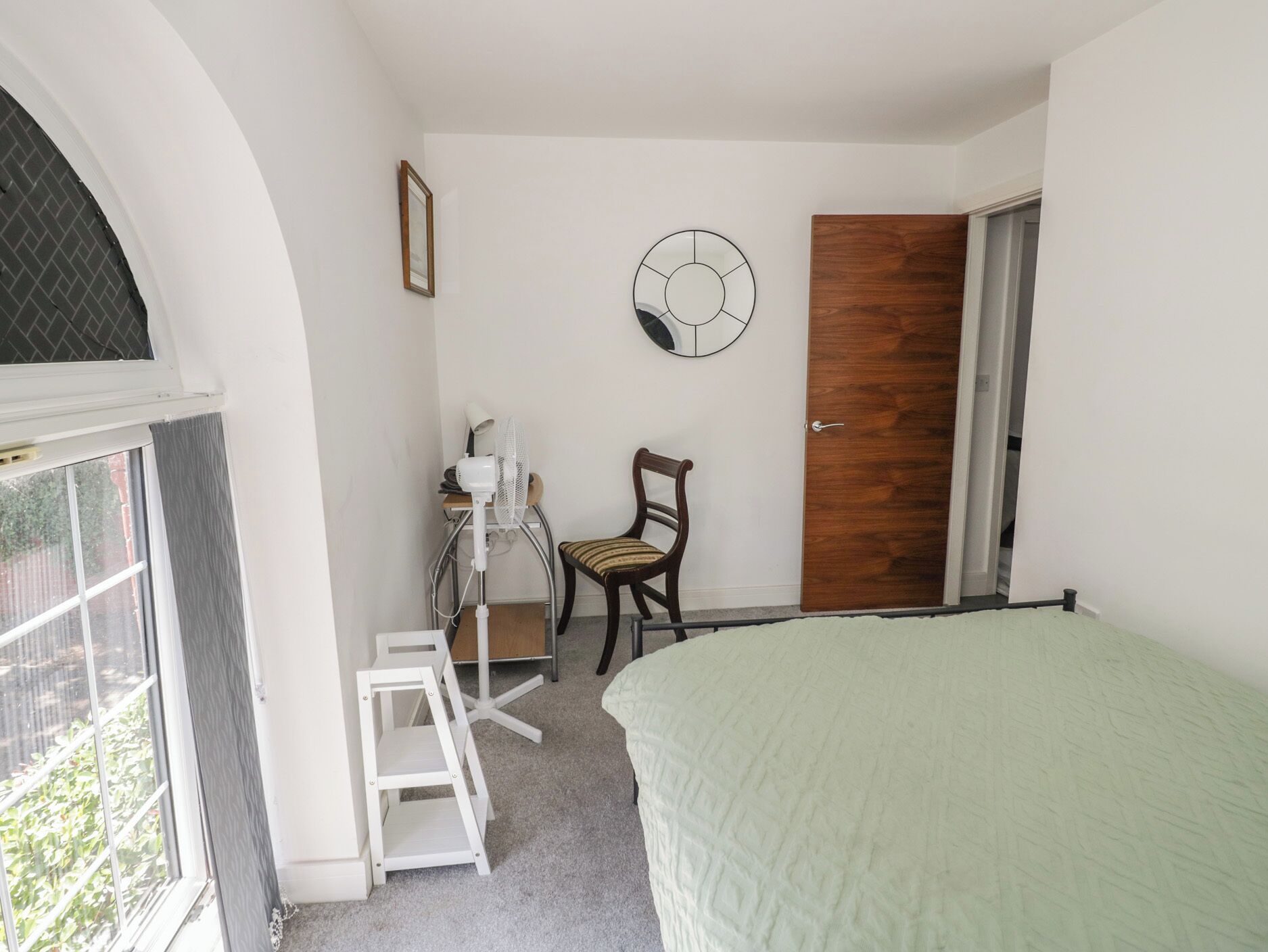 Un dormitorio con cama, una silla, un escritorio con otra silla, una puerta y una ventana.