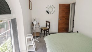 A bedroom with a bed, a chair, a desk with a chair, a door, and a window.