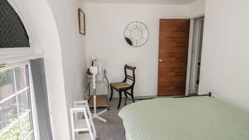 Un dormitorio con cama, una silla, un escritorio con otra silla, una puerta y una ventana.
