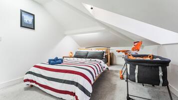A bedroom with a sloped ceiling, a bed with striped bedding, a nightstand with a lamp, and a baby stroller.