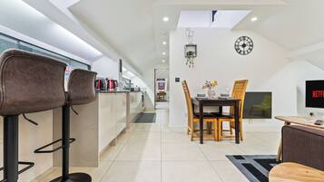 A modern kitchen with a dining area, a TV, and a clock on the wall.