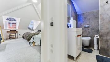A bedroom with a sloped ceiling, a desk, a bed with patterned bedding, and a window.