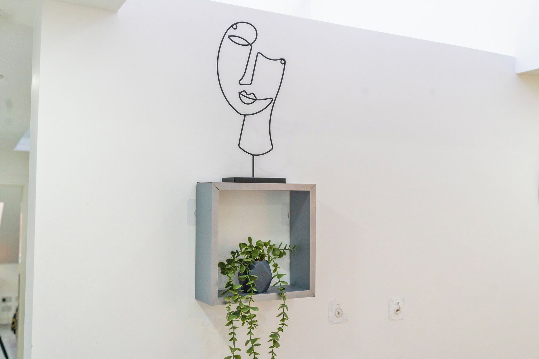 A minimalist wall with a simple line drawing, a small shelf with a plant, and a wall-mounted light fixture.