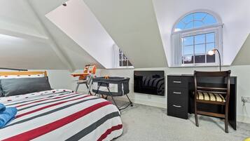 A bedroom with a sloped ceiling, a bed with striped bedding, a desk with a chair, a wardrobe, and a window with a view.