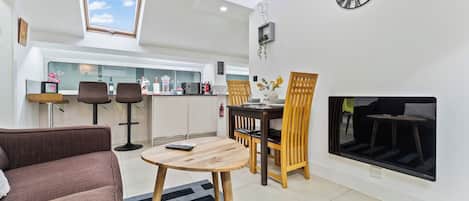 A modern living room with a sofa, a dining table with chairs, a fireplace, and a kitchen in the background.