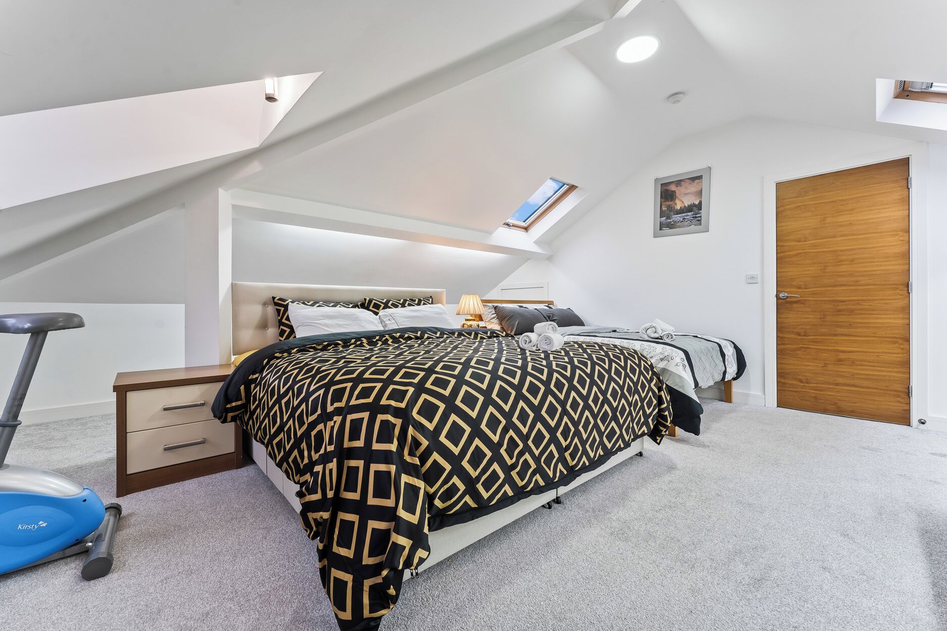 Une chambre à coucher comprenant un lit, un bureau, une chaise, un tapis de course et une lucarne.
