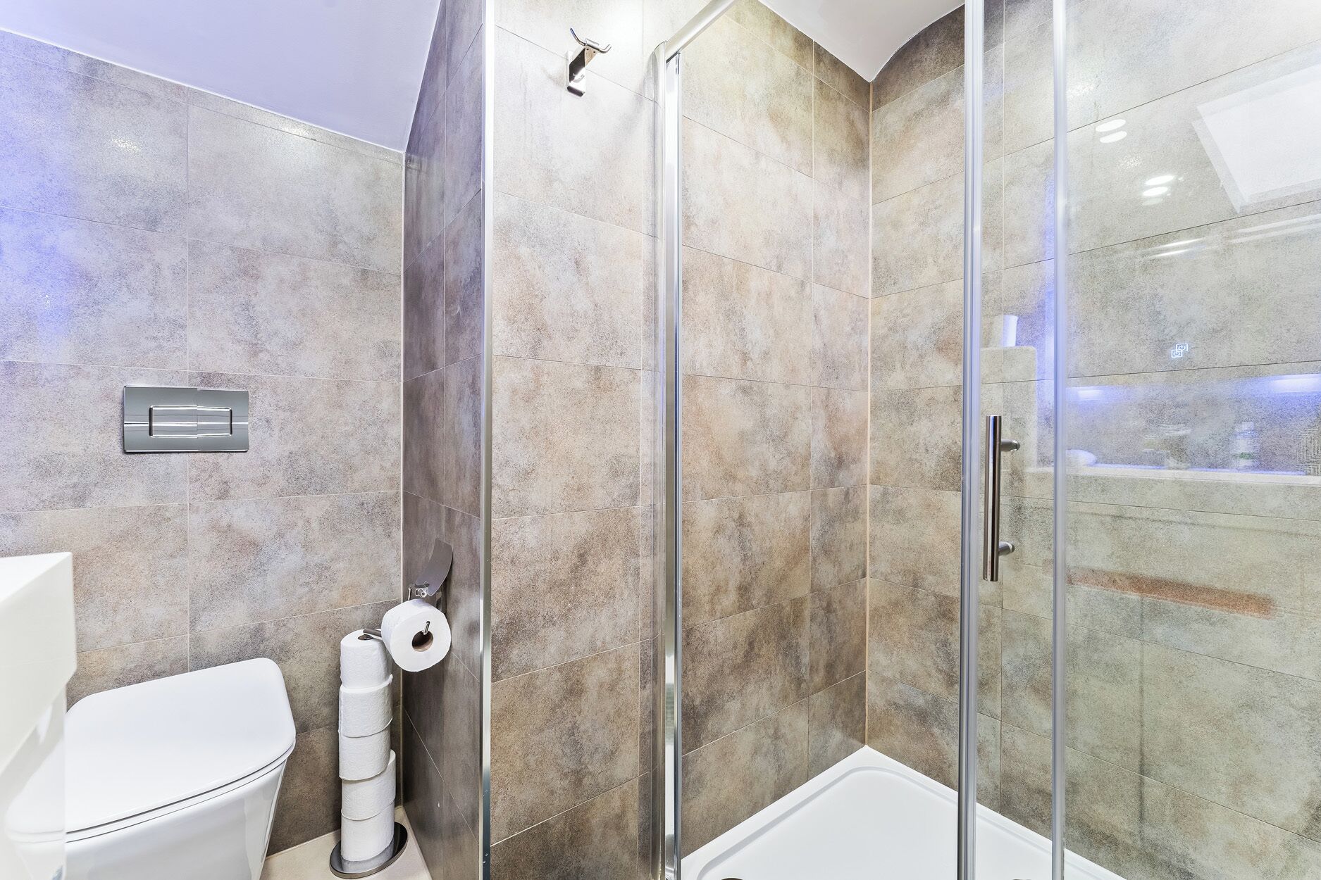 Un baño moderno con cabina de ducha de vidrio, inodoro y rollo de papel higiénico.
