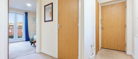 A corridor with wooden doors, a carpeted floor, and a view of an outdoor area with a blue curtain.