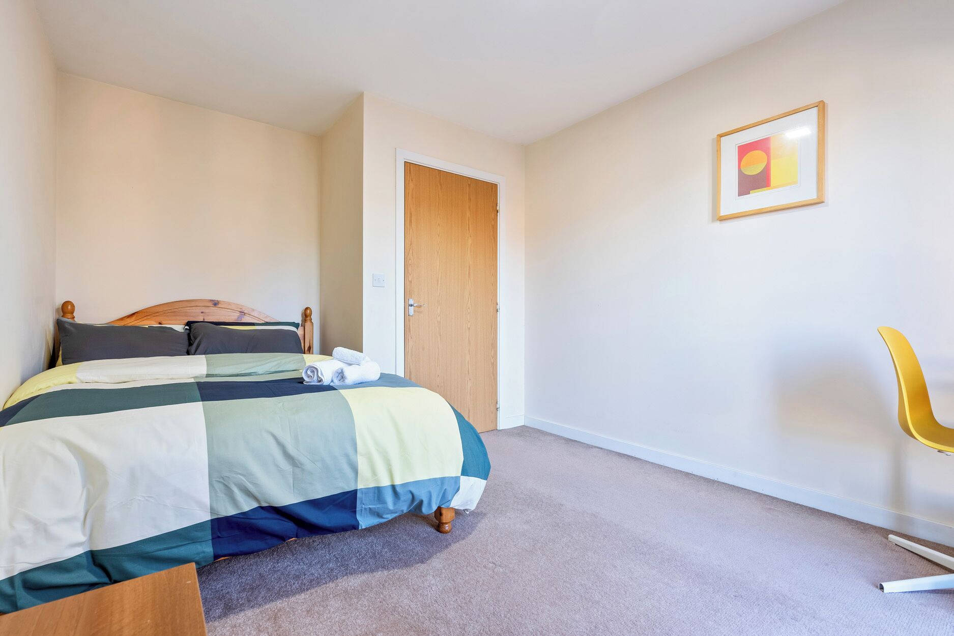 A bedroom with a bed, a wooden door, a framed picture on the wall, and a yellow chair.
