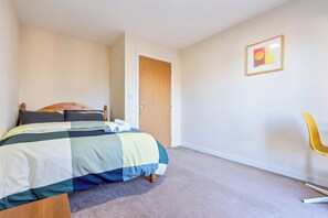 A bedroom with a bed, a wooden door, a framed picture on the wall, and a yellow chair. - Flat 34 Herbert James Close (Birmingham)