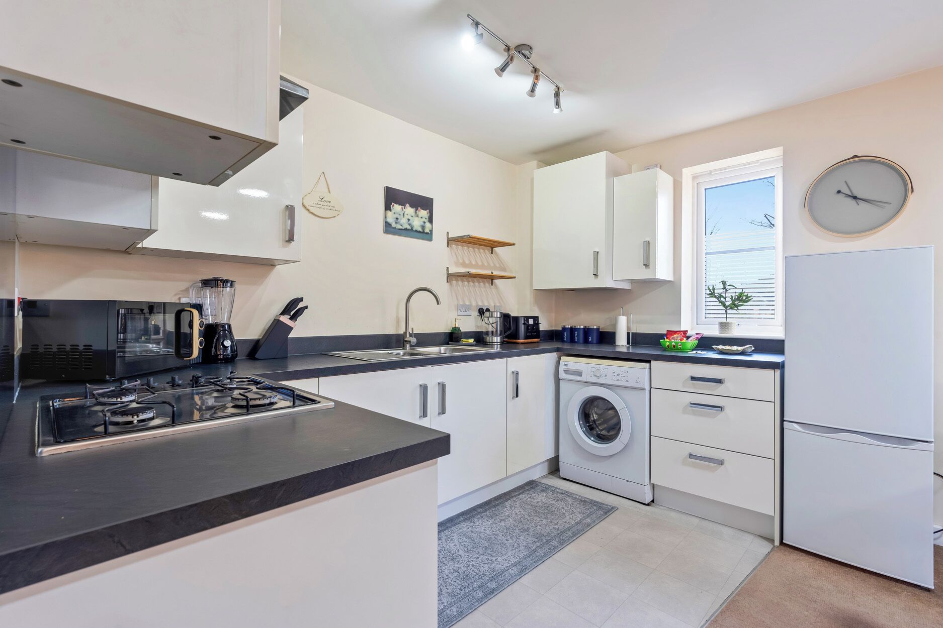 A modern kitchen with a gas stove, coffee maker, and a washing machine.