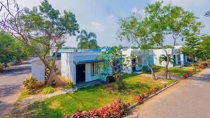 A row of modern, single-story buildings with a flat roof, surrounded by well-maintained grass and trees. - King Resort (Marakkanam)