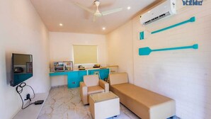 A compact room with a bed, a desk, a chair, a TV, and a ceiling fan. - King Resort (Marakkanam)