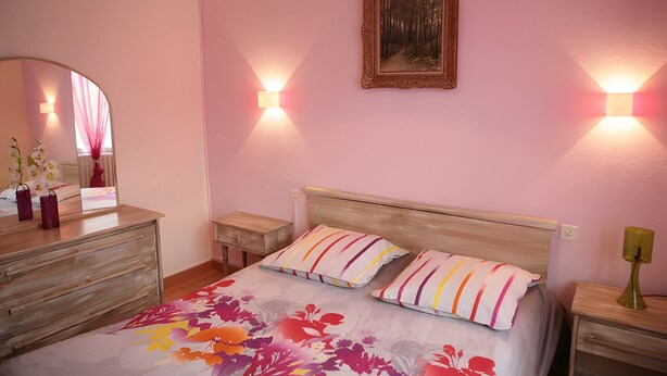 Un dormitorio con cama, cómoda, espejo y dos luces fijadas a la pared.