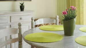 Una mesa de comedor con individuales verdes, una planta en maceta con flores rosas y un adorno de pared.